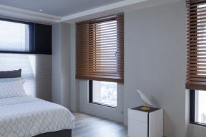 A picture of a bedroom with a twin-sized bed on the left and a set of brown horizontal blinds on the right.