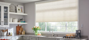 A picture of a kitchen with a big window over the sink with white shades