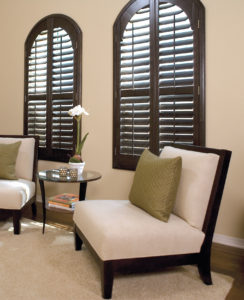 A room in a home with two arch-shaped windows that have brown plantation shutters.