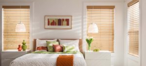 A bright bedroom with a queen-sized bed and windows lining the walls with blinds