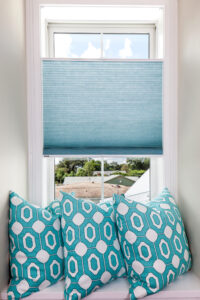 Picture of blue window shades installed on a window, above a window seat with blue pillows on it.